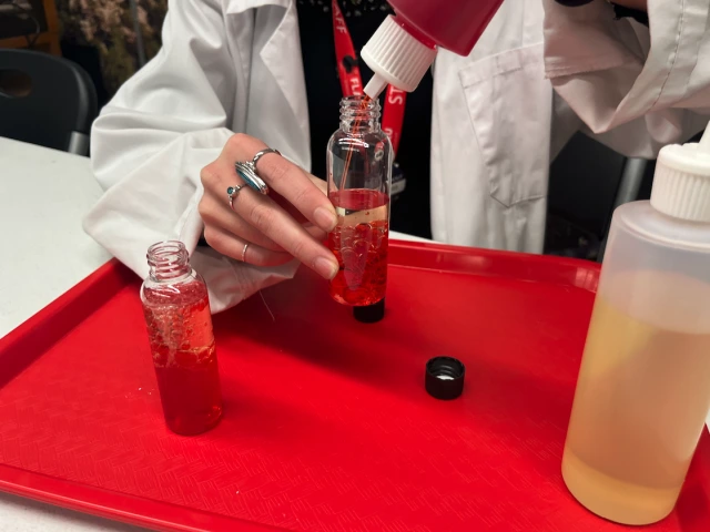 Staff member pours red liquid into yellow liquid 